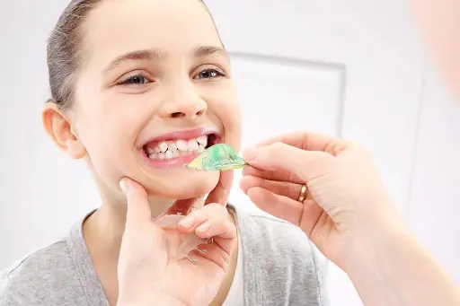 A woman is brushing her teeth with an apple green toothbrush.